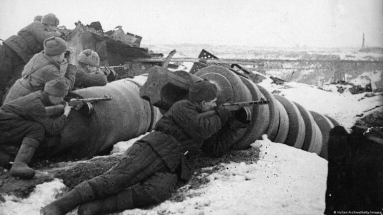 Black and white photograph of soldiers operating artillery in snowy, rubble-strewn terrain