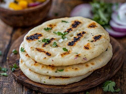 Stack of three cornmeal flatbreads with charred spots and fresh herbs on wooden board