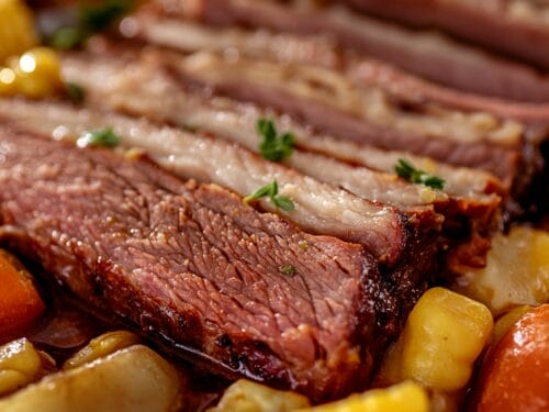 Sliced cooked meat with herb garnish nestled among boiled potatoes and root vegetables