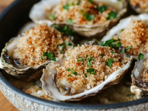 Oysters in shells topped with golden breadcrumb mixture and chopped parsley on plate