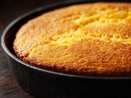 Golden-brown baked cornbread in cast iron skillet with textured, crumbly surface