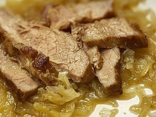 Close-up of cooked pork chunks nestled in pale, translucent cabbage strands in broth