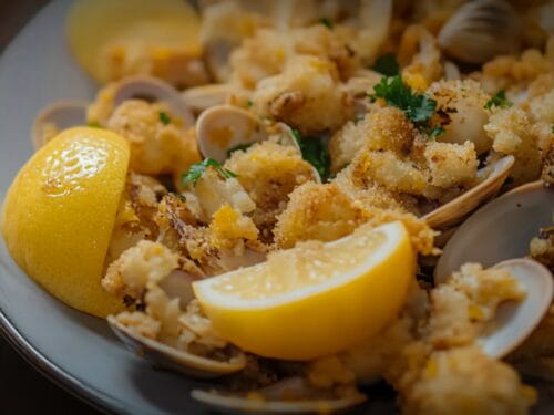 Golden-brown fried clams on a plate with lemon wedges and parsley garnish