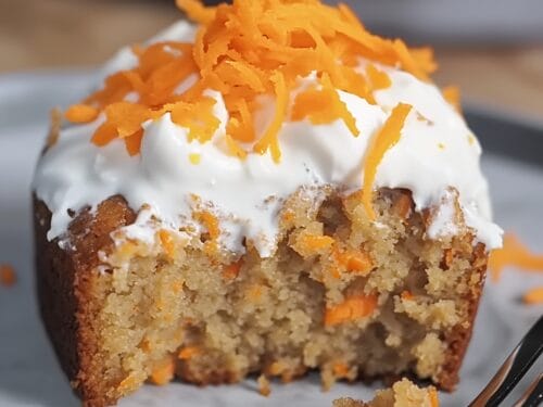 Spiced cake studded with carrot pieces, topped with white frosting and candied carrot ribbons