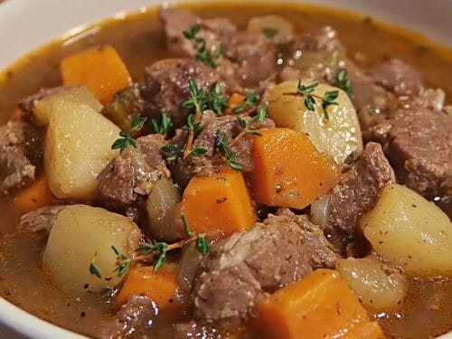 Beef chunks with diced potatoes and carrots in brown broth, garnished with fresh herbs