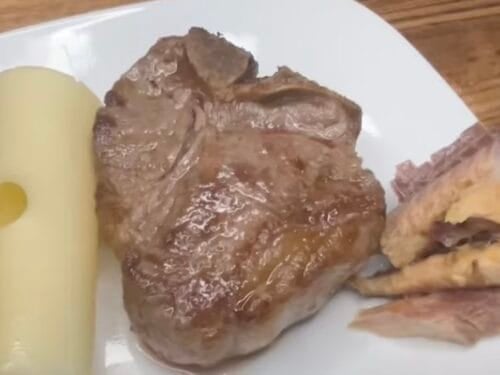 Plate with cooked meat chop, Swiss cheese cylinder, and fried potatoes on white plate