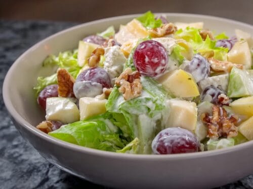 White bowl of salad with lettuce, apple chunks, red grapes, walnuts, and creamy dressing