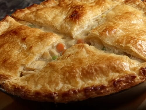 Baked pie with golden-brown crust split open to reveal creamy filling with visible carrot and pea pieces