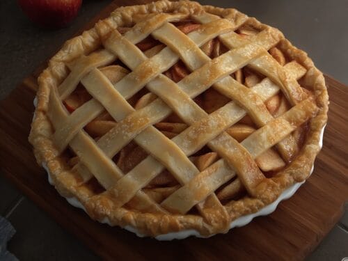 Golden-brown pie with lattice crust and crimped edge, filled with sliced apples, on wooden surface