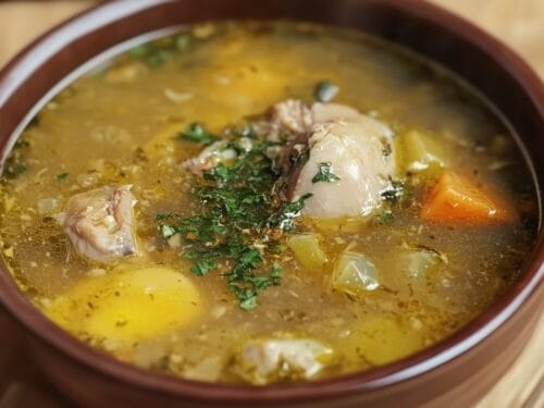 Bowl of broth with meat, vegetables, and fresh parsley garnish