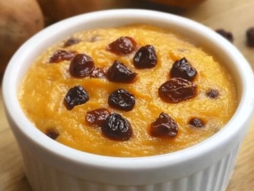 Golden-brown pudding in white ramekin topped with dark dried berries