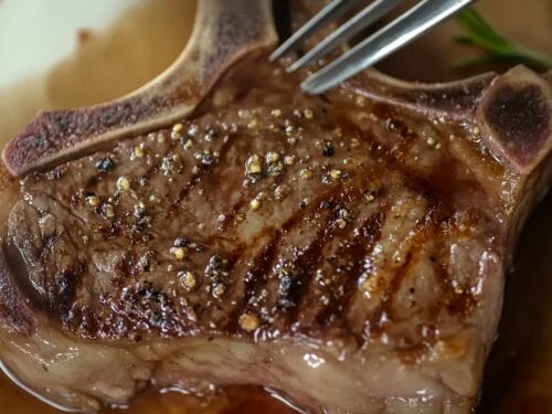 Seared steak topped with peppercorns, tongs resting on surface