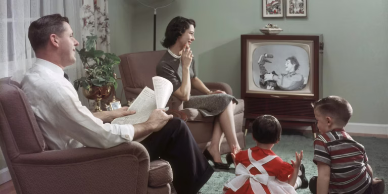 Family sitting in living room watching television, man holding newspaper, woman and two children on floor