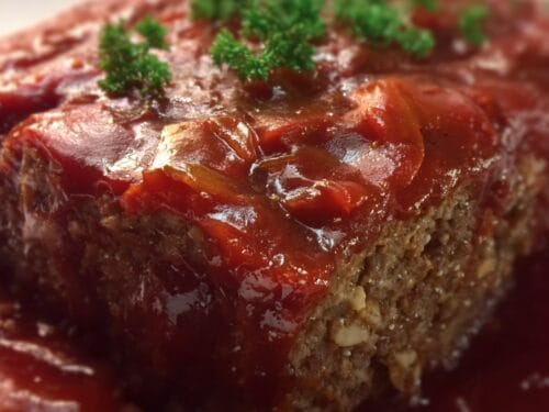 Cooked meatloaf slice with glossy red glaze and fresh parsley garnish