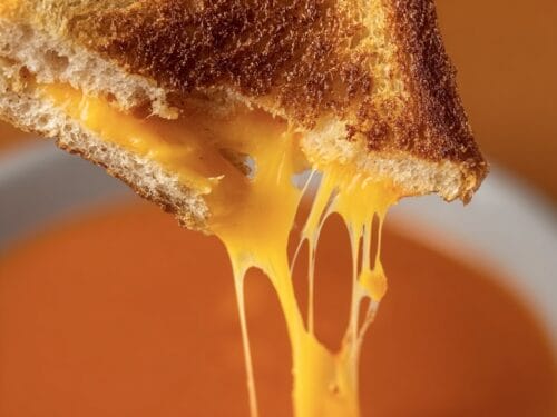 Toasted bread with melted yellow cheese stretching downward against warm orange background