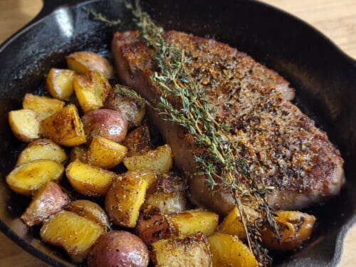 Seared steak with fresh rosemary sprigs and roasted potato chunks in cast-iron skillet