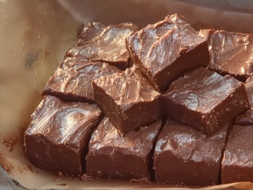 Brown fudge pieces stacked in tan baking dish with textured surface
