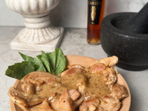 Cooked chicken pieces with sauce and mint leaves on wooden plate, amber bottle behind