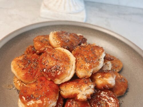 Caramelized fried dough balls scattered on beige ceramic plate, sprinkled with black seeds