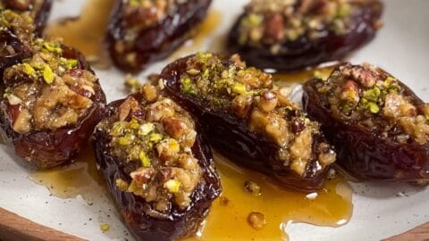 Dark dates filled with nuts and topped with pistachios, arranged on white plate with pooled oil