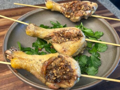 Four roasted small birds on skewers with spiced breadcrumb coating and parsley on gray plate