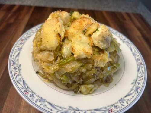 Layered dish of cabbage and potatoes with golden-brown top on decorative blue-rimmed plate