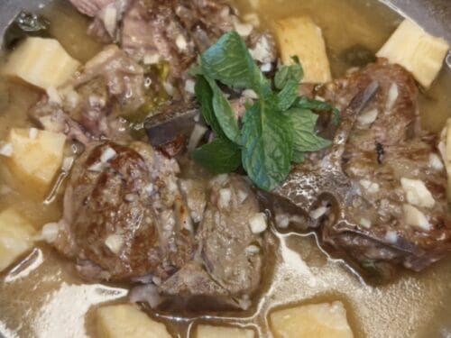 Cooked lamb pieces and cubed potatoes in savory broth, garnished with fresh mint