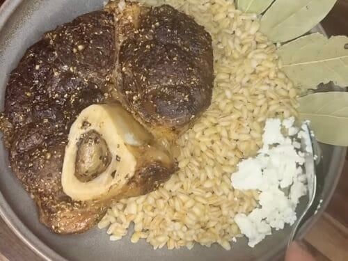 Roasted meat with herbs on a plate alongside rice and crumbled white cheese
