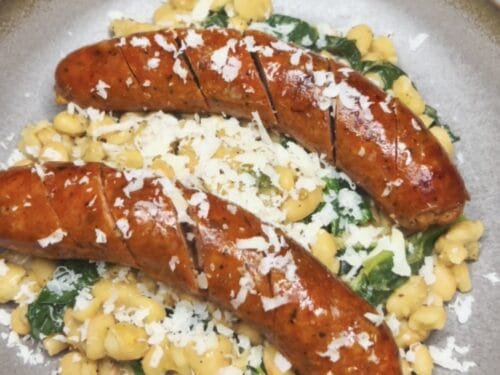 Two browned sausages topped with grated cheese on corn and greens