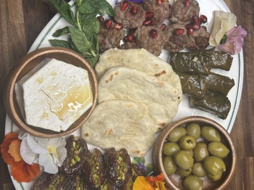 White plate with meatballs, flatbread, stuffed grape leaves, olives, cheese, fresh mint, and edible flowers