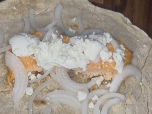 Flatbread wrap filled with meat, white cheese crumbles, and sliced onions