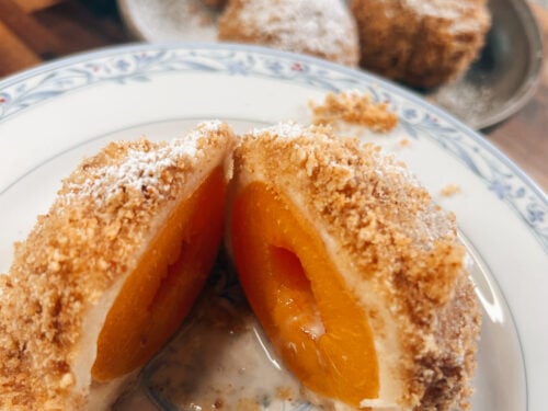 Halved pastry dumpling with cinnamon sugar coating reveals bright apricot filling inside