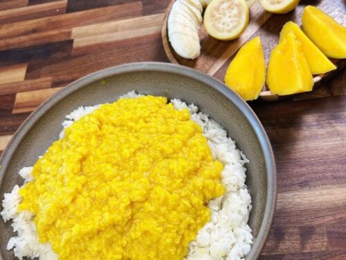 Yellow lentil curry over white rice in a bowl, with sliced banana, lemon wedges nearby