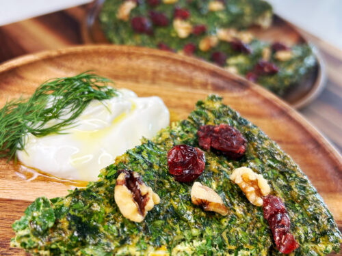 Green herb frittata slice topped with walnuts and dried berries, served with yogurt