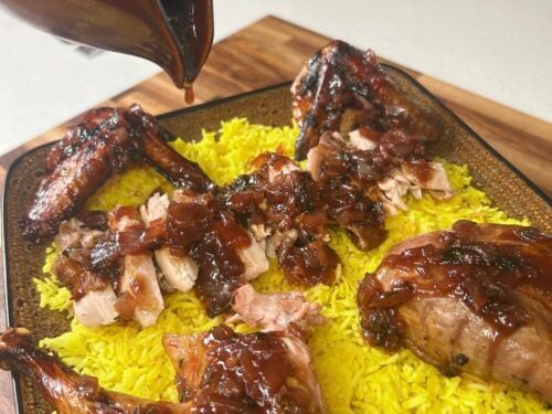 Dark sauce poured over roasted poultry and shredded yellow rice on a textured ceramic plate