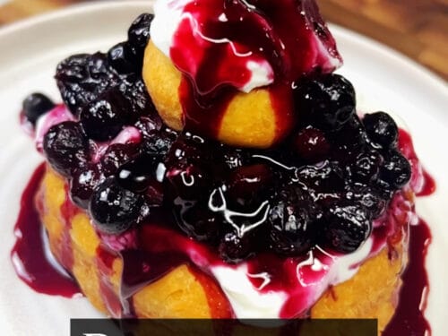 Papanași stacked on white plate, drizzled with dark fruit syrup and topped with black berries