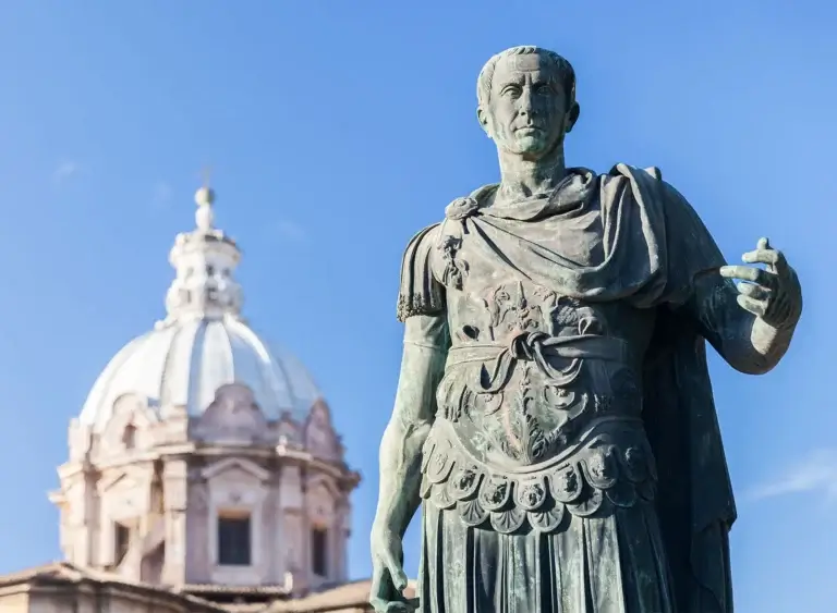 Stone statue of a robed figure in armor against blue sky, with domed building behind