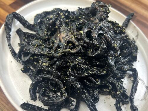 Cooked octopus with dark sauce and gold dust on white plate, wooden surface behind