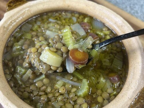 Earthenware bowl of lentil soup with leeks and diced carrot, spoon resting inside