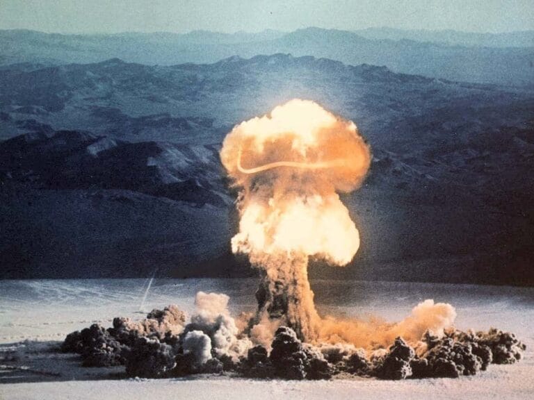 Nuclear explosion mushroom cloud rising above desert mountains