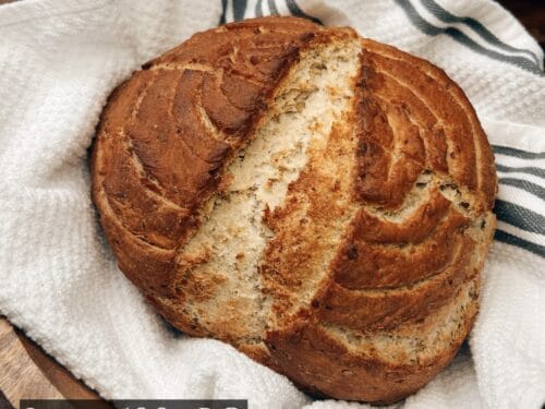Tan and brown loaf with visible seeds and scoring marks rests on cream linen with dark stripes