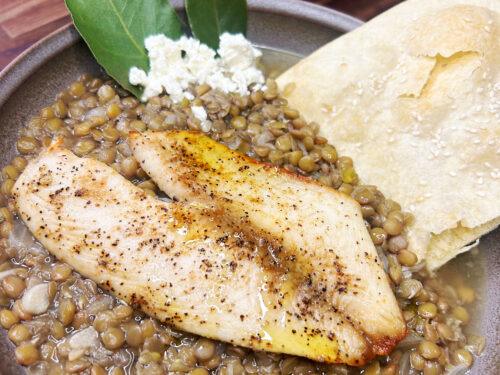 Cooked fish fillet on lentil stew with flatbread and fresh cheese on ceramic plate