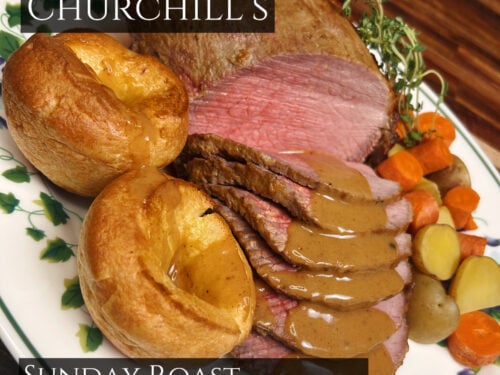 Sliced roast beef with golden Yorkshire puddings, gravy, roasted vegetables and fresh herbs on white plate