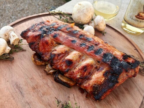 Glazed ribs with charred surface on wooden board with mushrooms and herbs