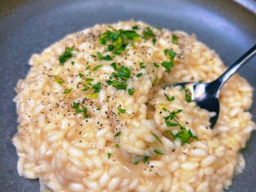 Creamy rice dish in gray bowl, topped with black pepper and fresh green herbs