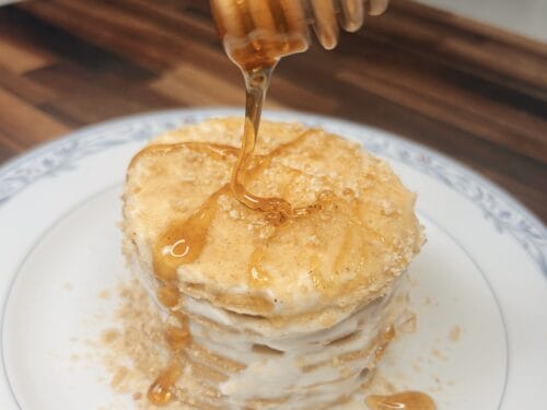 Honey drizzles from a wooden dipper onto a layered cake with cream filling on a white plate
