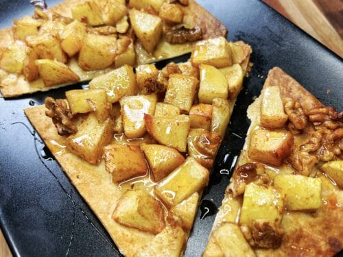 Baked flatbread wedges topped with diced apples, walnuts, and glossy honey glaze on black plate