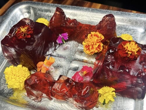 Deep red jelly molded in irregular shapes, garnished with yellow and pink flowers on a silver tray