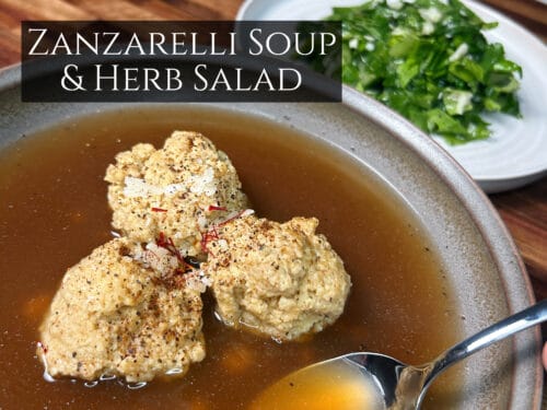 Zanzarelli soup with two dumplings in golden broth, fresh herb salad on white plate beside it