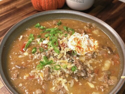 Brown stew with ground meat and beans, topped with sour cream, green onions, and paprika